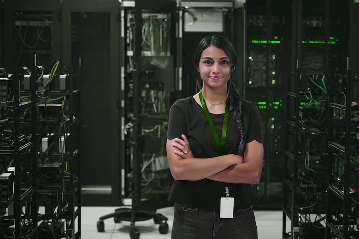 Person standing in a server room with their arms crossed